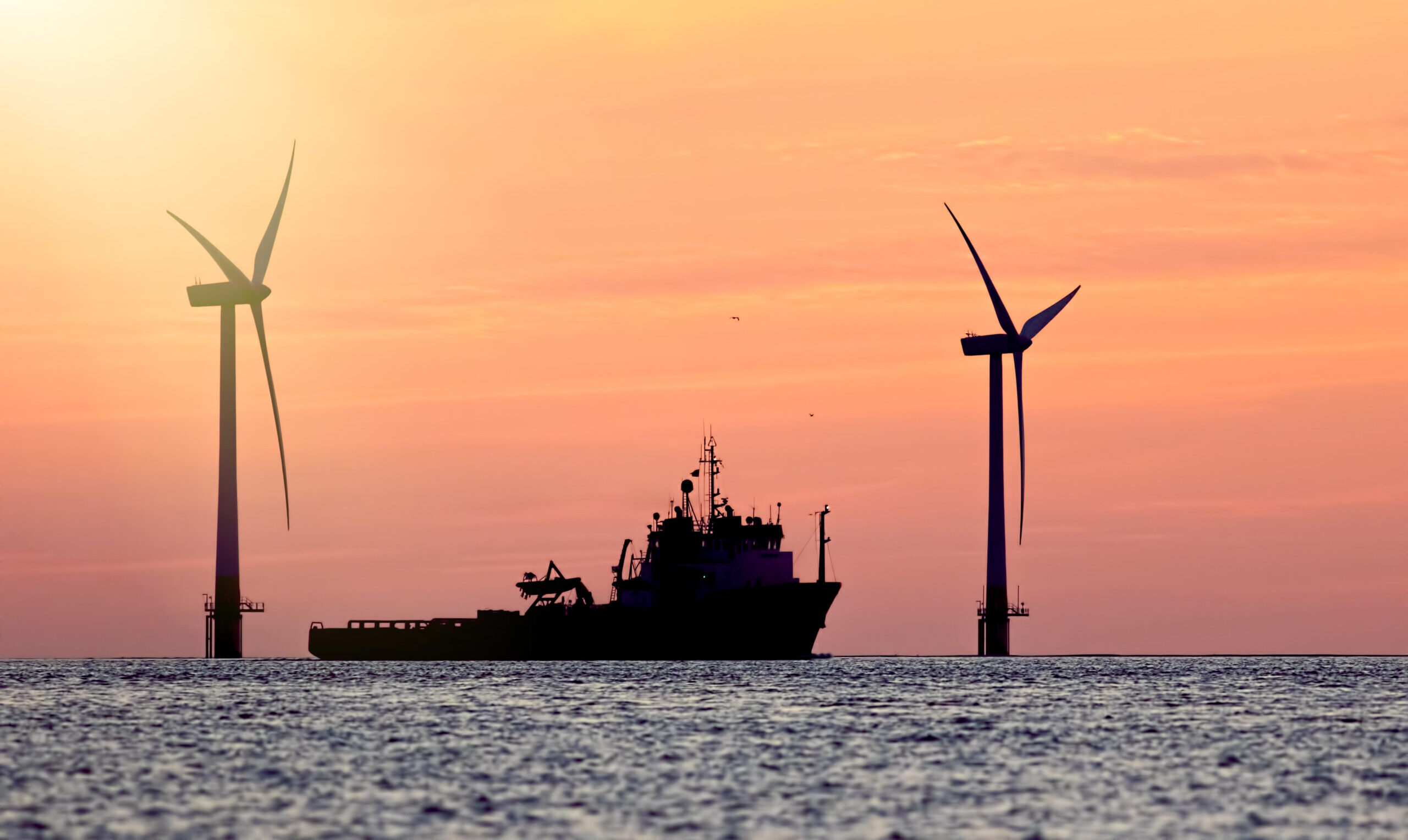 Sustainable resources. Wind farm with ship silhouette at tropical sunrise or sunset. Solar and wind energy and food supply represented in this tranquil image with copy space.